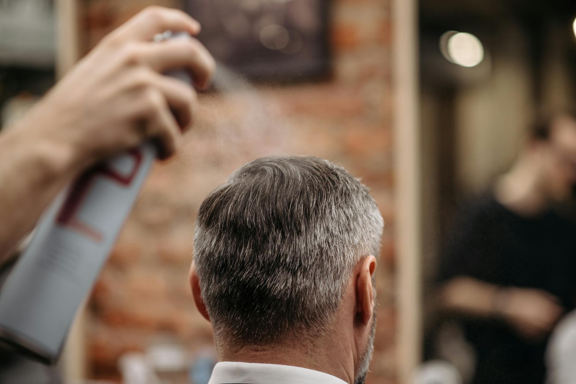 Fryzjer stylizuje włosy mężczyzny lakierem w nowoczesnym barbershopie