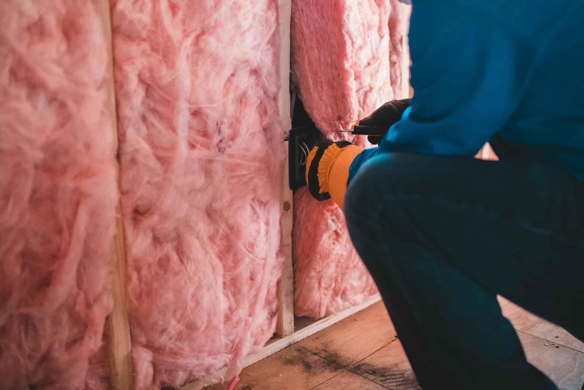 Jak zaplanować kompleksową termomodernizację domu krok po kroku i naprawdę obniżyć rachunki za energię Pracownik w rękawicach montuje różową wełnę mineralną w ścianie