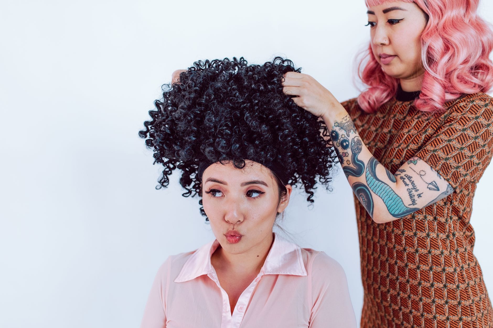 Stylista dopasowuje kręconą czarną perukę kobiecie w salonie