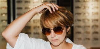 Kobieta w białej bluzce przymierza okulary przeciwsłoneczne w salonie optycznym